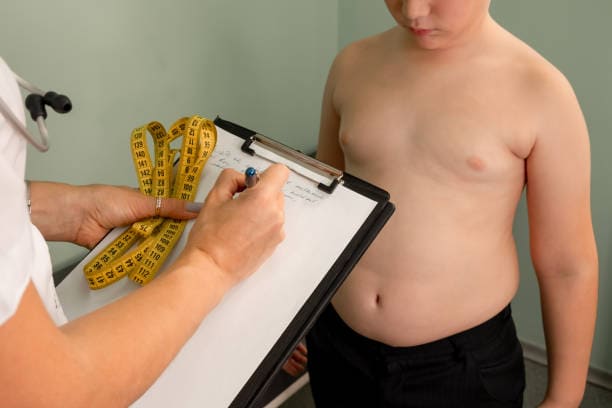Anak laki-laki kelebihan berat badan berkonsultasi dengan dokter / iStockphoto