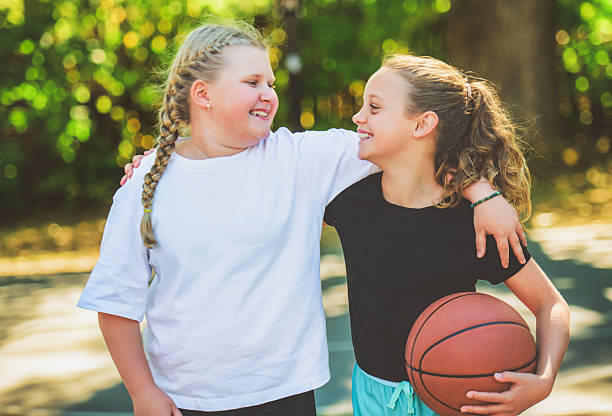 Dua anak perempuan dengan pakaian olahraga bermain bola basket di luar / iStockphoto