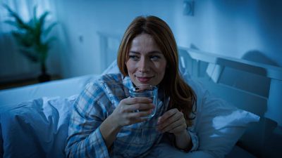 Seorang wanita sedang minum air putih sebelum tidur / iStockphoto