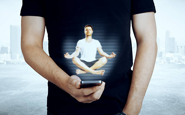 Pria kasual memegang ponsel dengan hologram orang bermeditasi abstrak / iStockphoto
