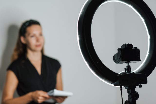 Seorang vlogger wanita merekam konten di dalam ruangan menggunakan kamera dan lampu cincin LED / pexels-anete-lusina