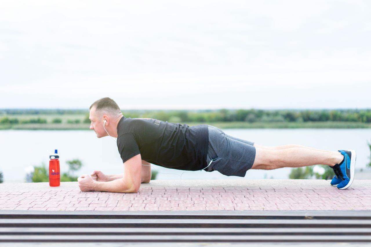 Pria berpakaian olahraga melakukan latihan plank di luar ruangan dekat danau / pexels-freestockpro