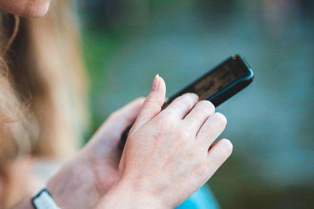 Tangan yang memegang smartphone dengan latar belakang kabur / pexels-introspectivedsgn