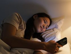 Seorang wanita berbaring di tempat tidur di malam hari menggunakan smartphone / pexels-ron-lach