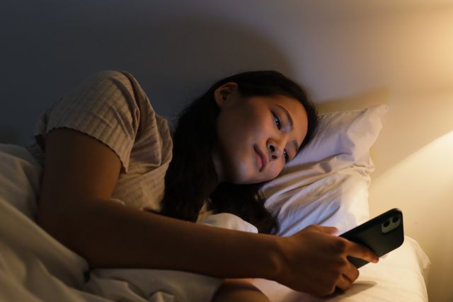 Seorang wanita berbaring di tempat tidur di malam hari menggunakan smartphone / pexels-ron-lach