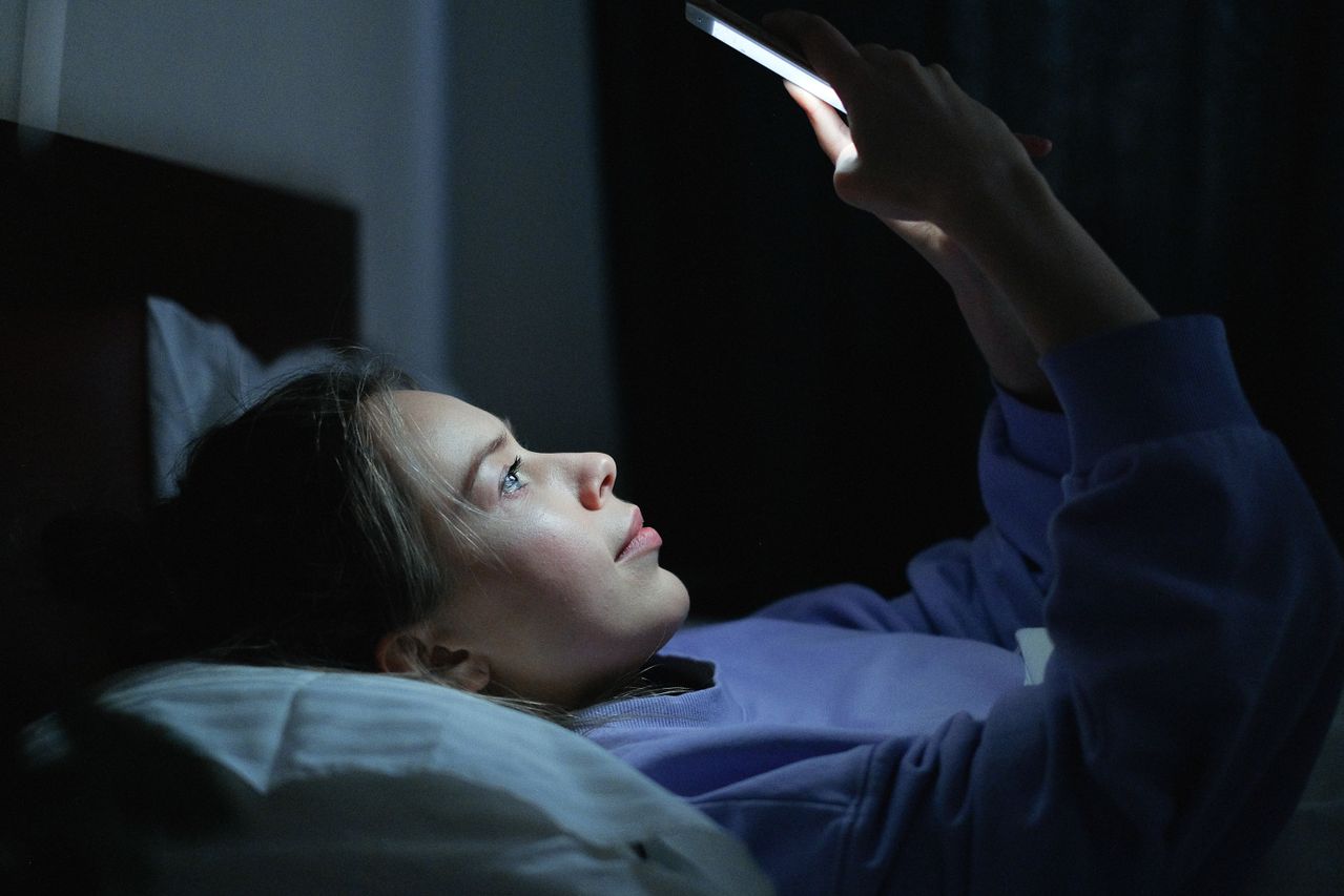 Wanita muda yang berbaring di ranjang menggunakan smartphone di malam hari / pexels-shvets-production